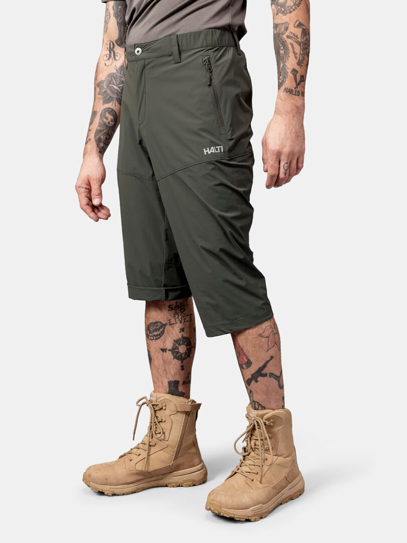 En person i Halti Pallas Cool X-stretch Capribyxor, grå skjorta, solbruna stövlar och tatueringar på armar och ben.
