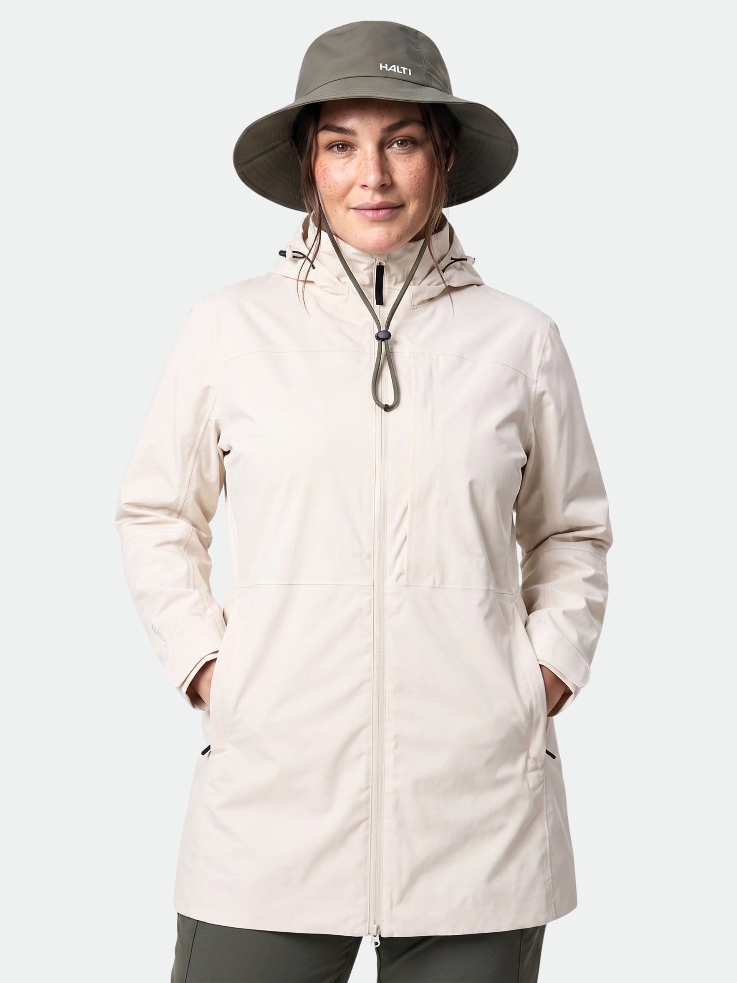 En person bär Halti Kallas DX Parka Plus Dam, med händerna i fickorna, framför en enfärgad bakgrund.
