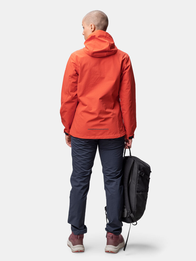 Person vänd bort, klädd i Halti Finholma X-stretch Jacka Dam, mörka byxor och med en svart ryggsäck i höger hand.