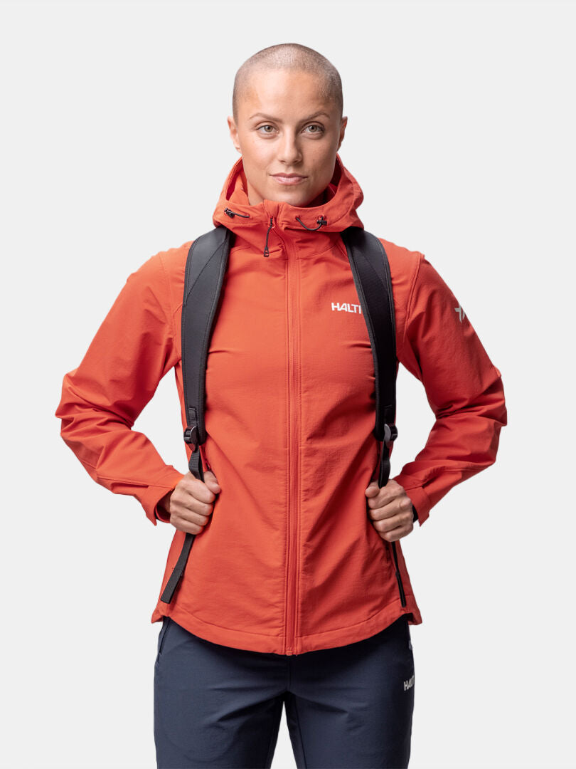 En person med rakat huvud bär en Halti Finholma X-stretch Jacka Dam och en svart ryggsäck mot en vit bakgrund.