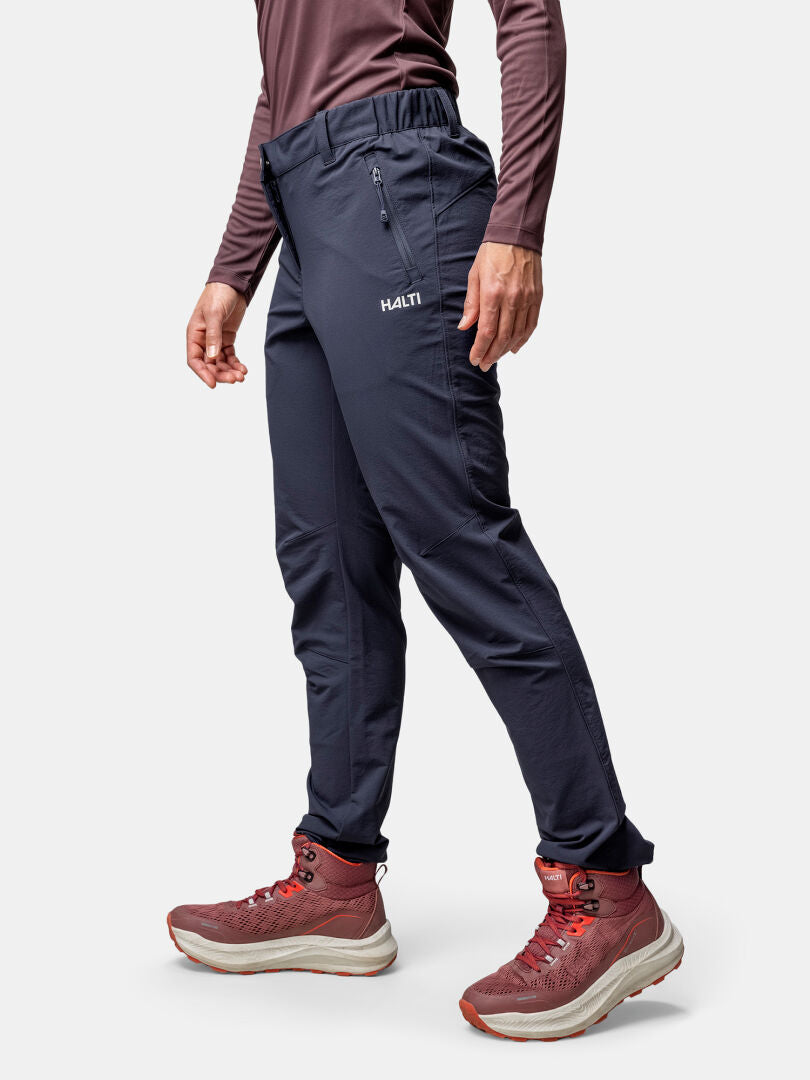 En person bär Halti Finholma X-stretch Byxor Dam, en rödbrun långärmad topp och matchande vandringskängor mot en enfärgad bakgrund.