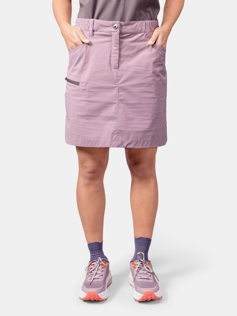 En person i Halti Pallas Cool Skjol Dam, lila strumpor och rosa sneakers står med händerna i kjolfickorna.