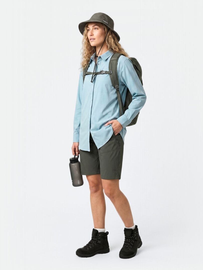 En person i Halti Samoy Långärmad Funktionsskjorta Dam, gröna shorts, vandringskängor, ryggsäck och med en vattenflaska i handen.