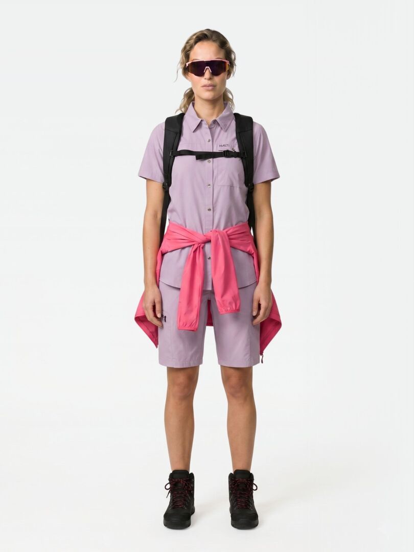 En person bär Halti Samoy Funktionsskjorta Dam med lavendelfärgade shorts, en rosa jacka i midjan, stövlar och solglasögon.