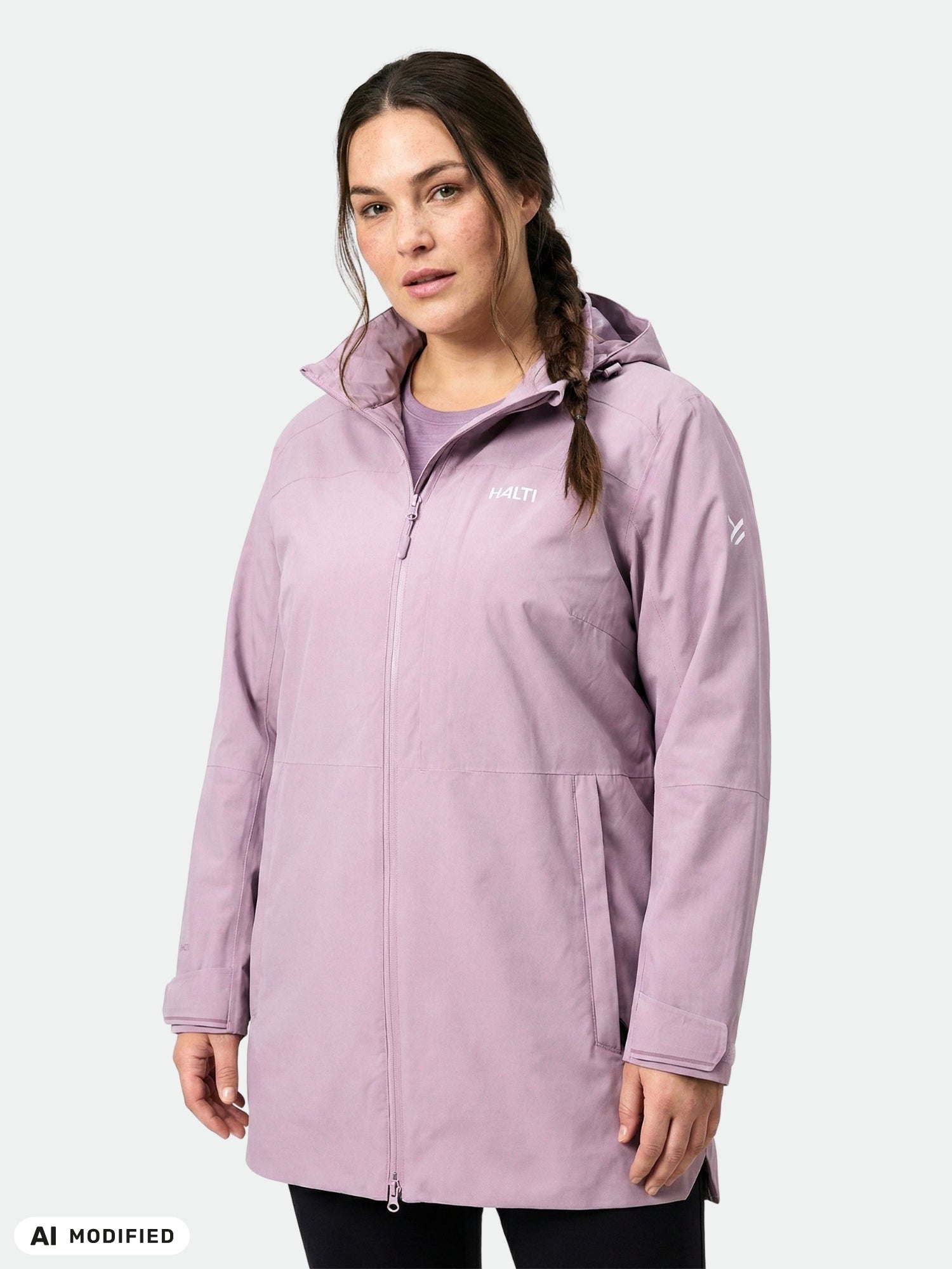 En kvinna i en Halti Valaja DX Parka Dam Plus, en lång ljuslila kappa med huva, står framför en enfärgad bakgrund.