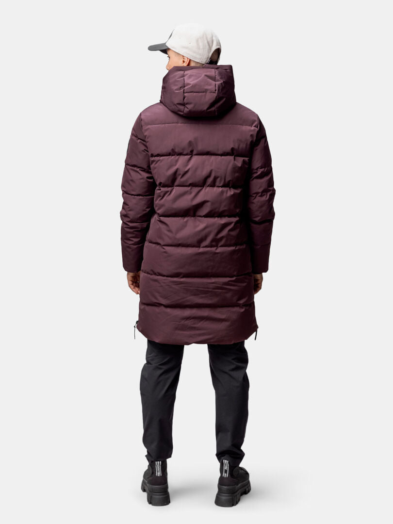 Person i rödbrun Halti Linjat Parka Jacka Dam, svarta byxor och skor, grå keps, står vänd bort.