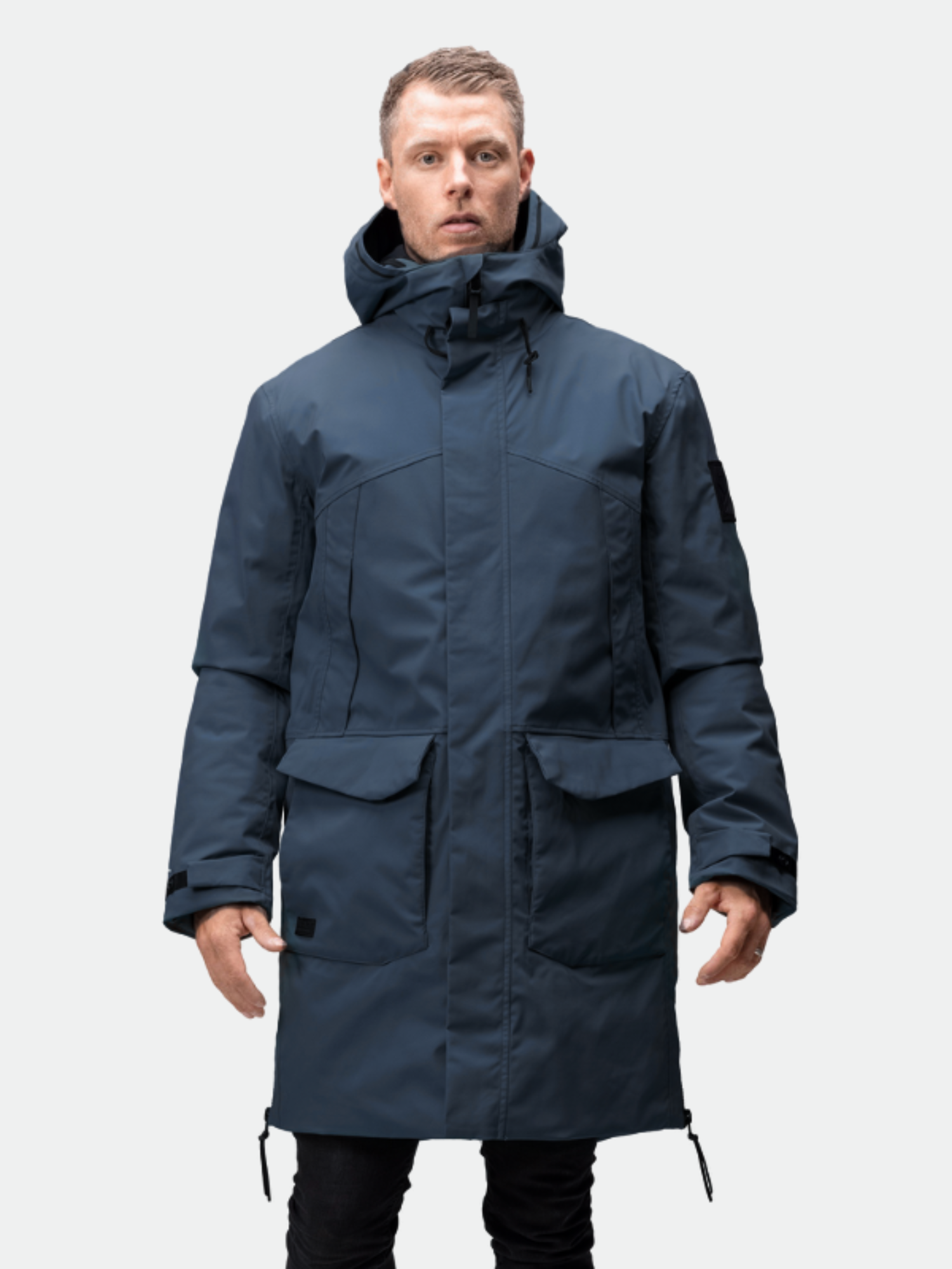 En man bär Halti Bergga Herr DrymaxX Vinterjacka och står vänd framåt mot en ljusgrå bakgrund.