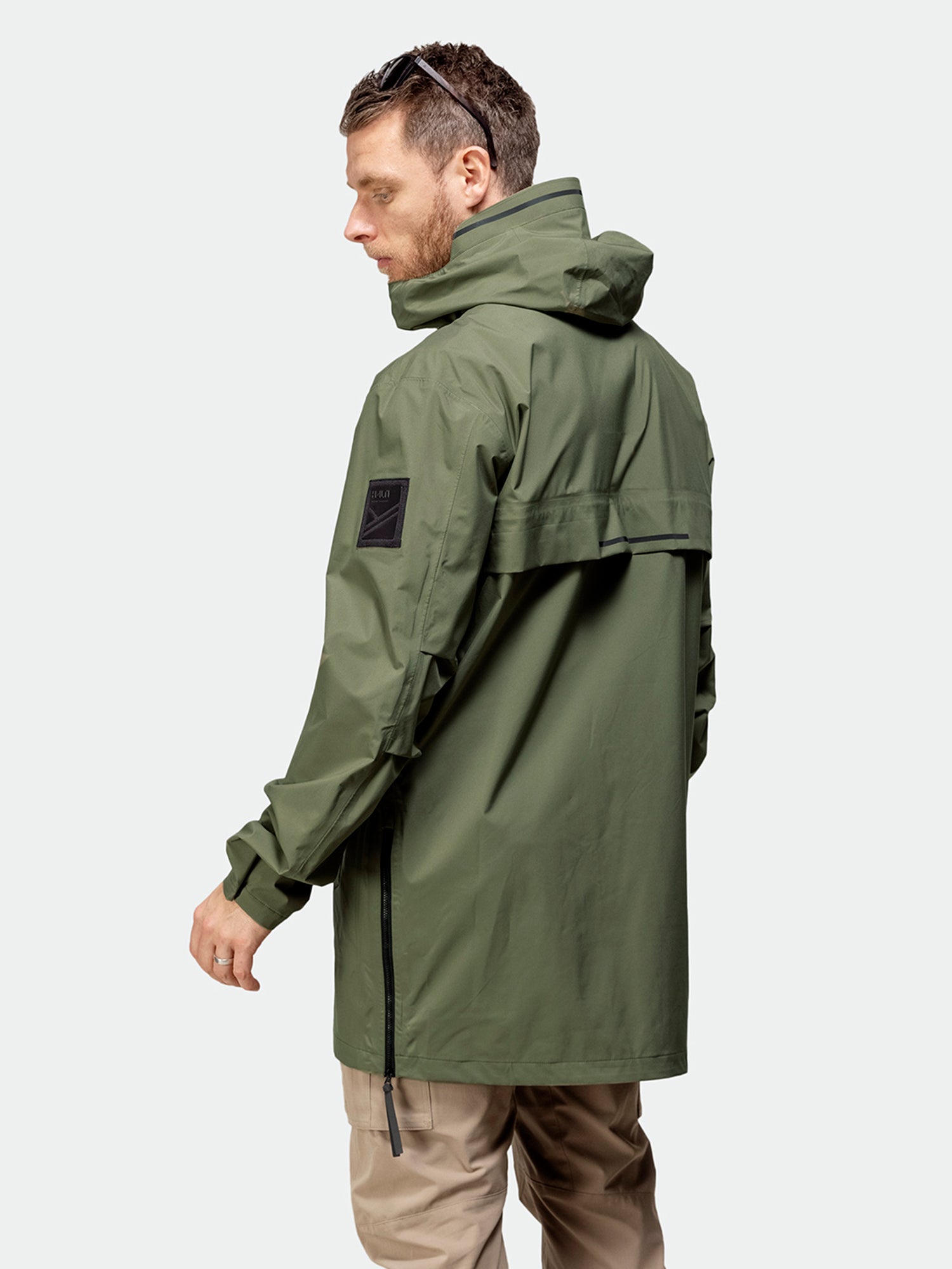 Man bär Halti Kurvi Herr DrymaxX 3L Parka Jacka i olivgrönt med beige byxor, från sidan, ljus bakgrund.