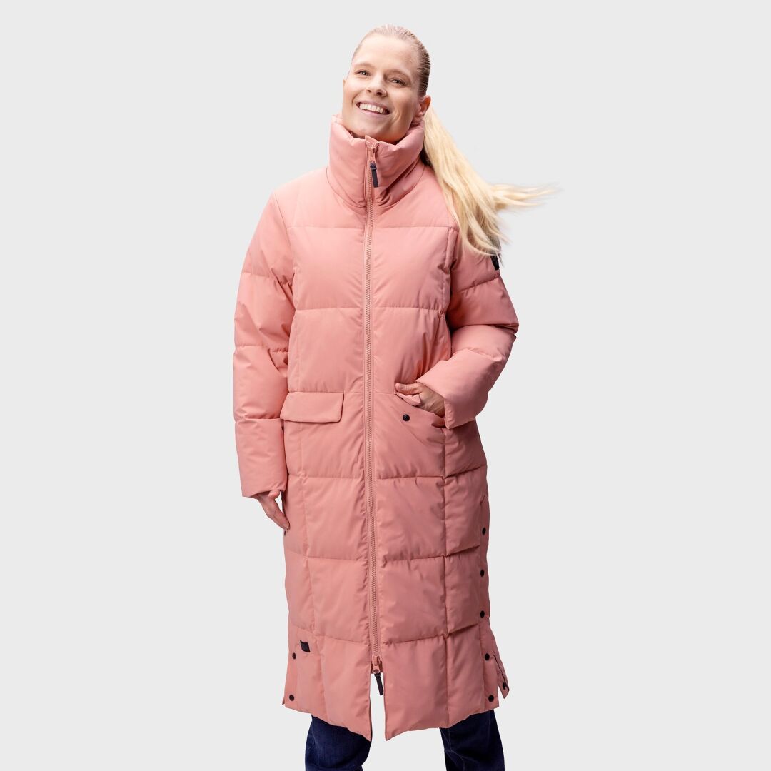 En kvinna bär den rosa täckjackan Halti Penger Vinterjacka Dam med händerna i fickorna, mot en enfärgad ljus bakgrund.