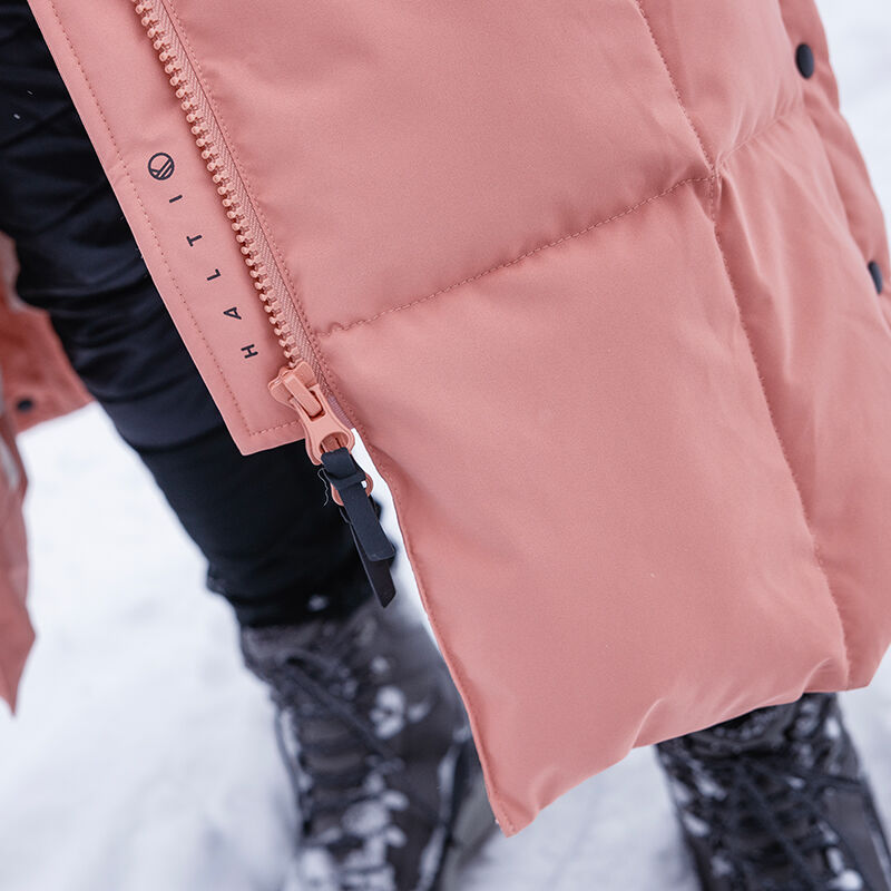Närbild av Halti Penger Vinterjacka Dam i rosa, buren på snö med svarta stövlar och med dragkedja.
