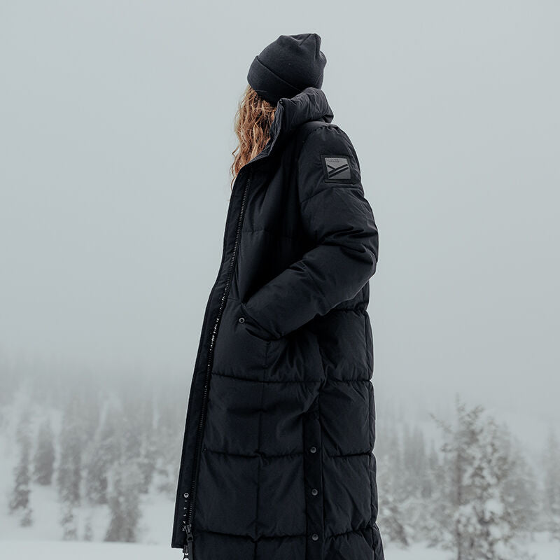 En person i en Halti Penger Vinterjacka Dam och mössa står utomhus i ett snöigt, dimmigt landskap med träd bakom.