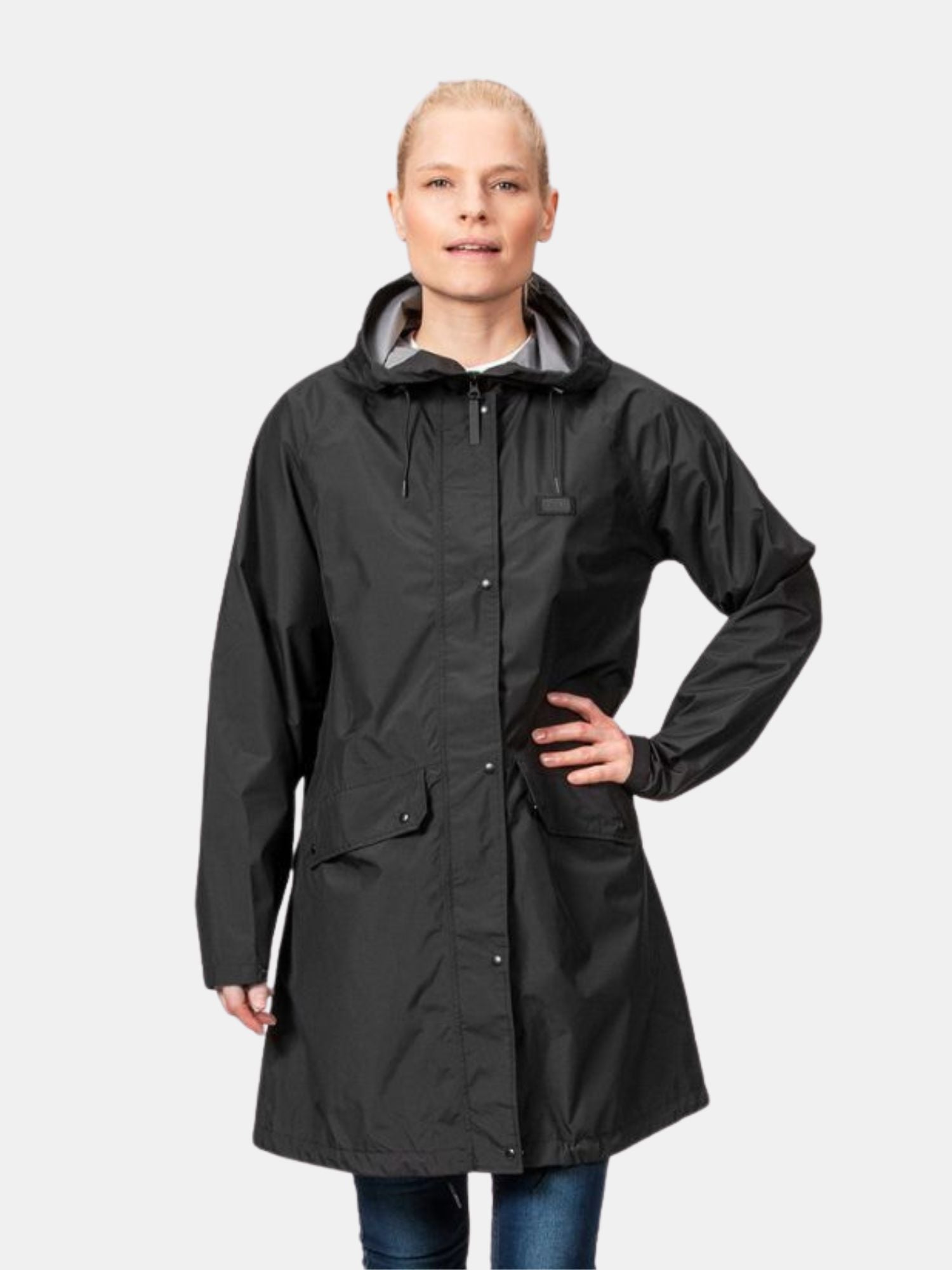 En kvinna bär Halti Kevee Parka Jacka Dam, stående med ena handen på höften mot en enfärgad bakgrund.
