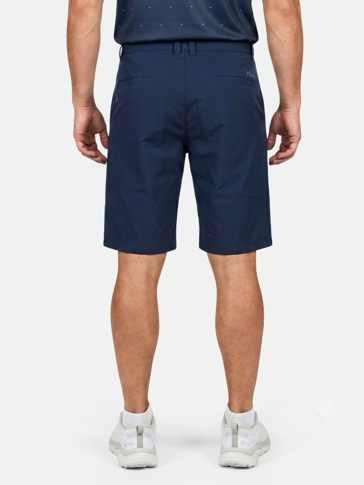 En man bär Halti Drive X-stretch Shorts Herr i marinblått tillsammans med en marinblå skjorta och vita sneakers mot en vit bakgrund.