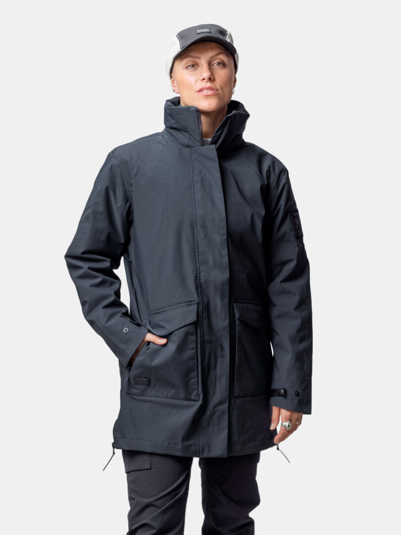 Person iklädd Halti Synkas 3in1 DrymaxX Parka Dam, ljus keps och mörka byxor, står mot en ljus bakgrund.