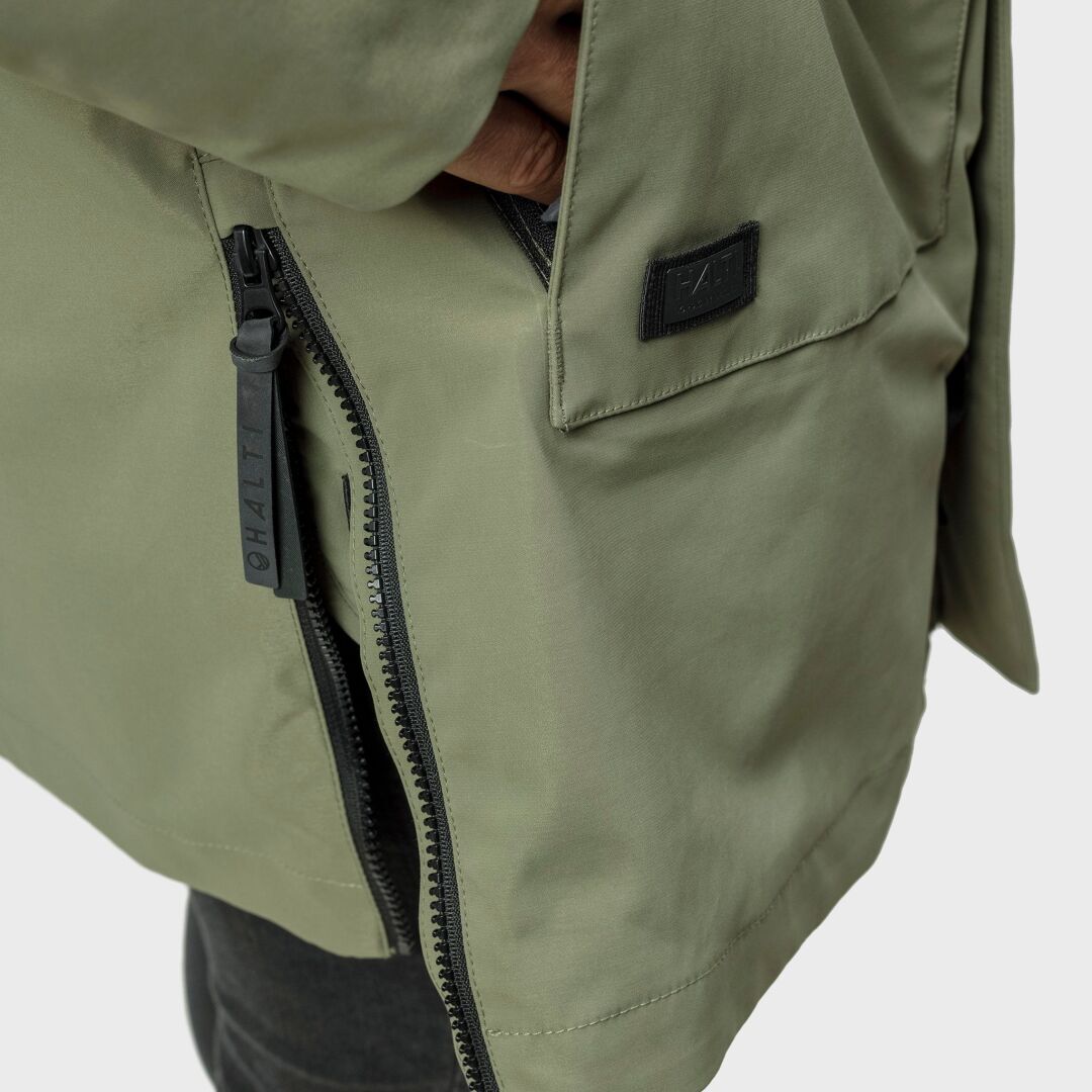 Närbild på en khakifärgad Halti Synkas 3in1 DrymaxX Parka Herr som visar en hand i fickan, dragkedja och svart lappdetalj.