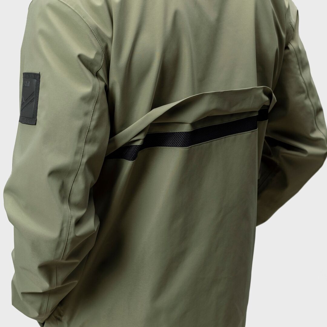 En person bär en Halti Synkas 3in1 DrymaxX Parka Herr, olivgrön med svart rand och lapp på vänster ärm, sedd bakifrån.