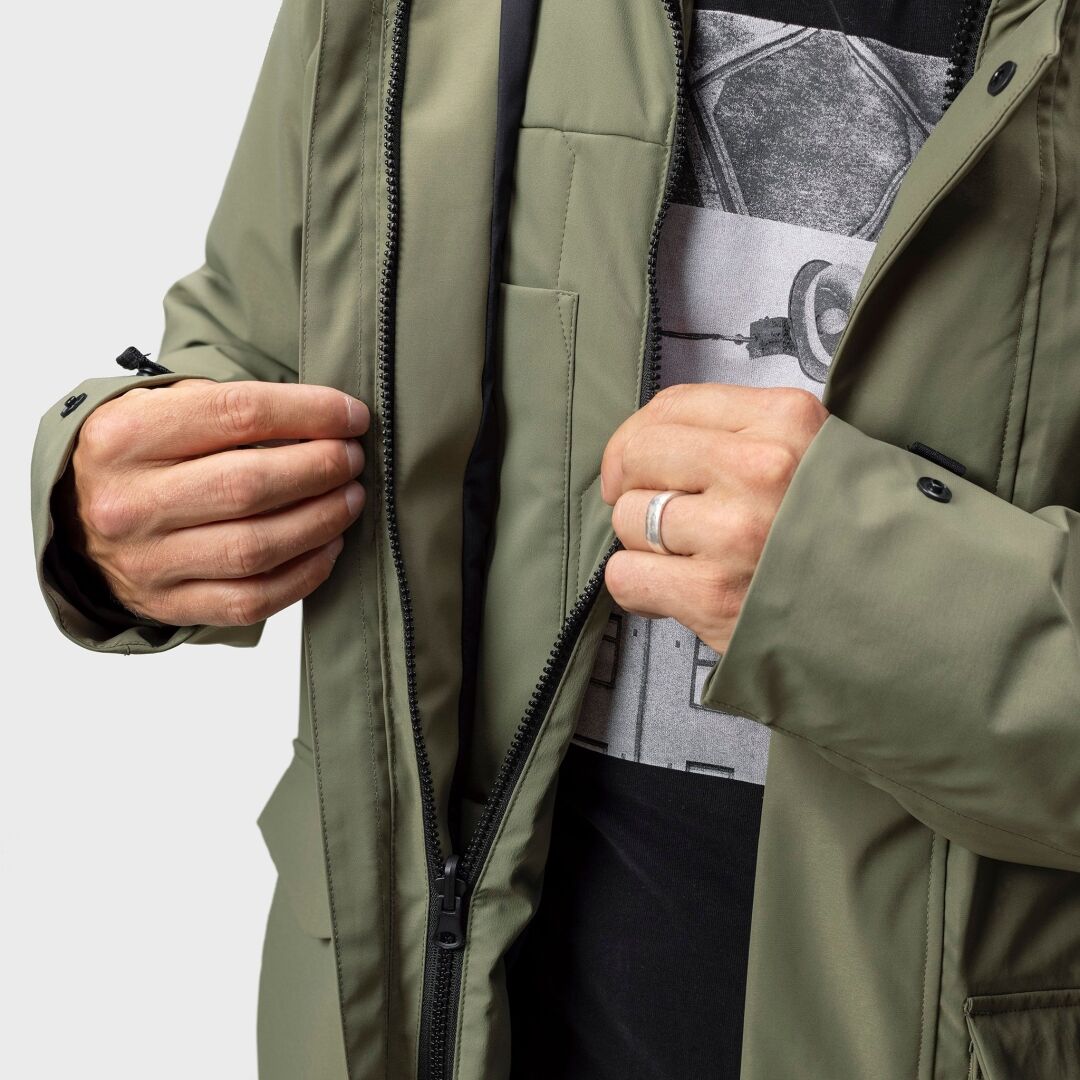 Någon i en Halti Synkas 3in1 DrymaxX Parka Herr (olivgrön) öppnar dragkedjan och avslöjar en svart skjorta med kameratryck.