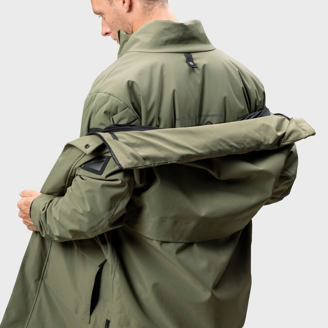 En person i en Halti Synkas 3in1 DrymaxX Parka Herr öppnar en dragkedja baktill, sett över axeln.