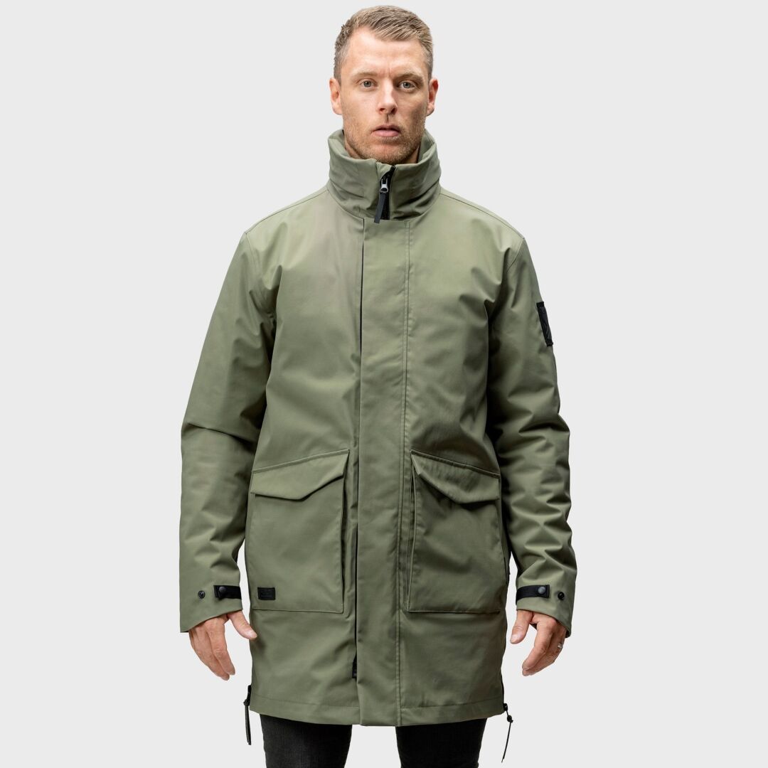 En man vänd framåt och bär Halti Synkas 3in1 DrymaxX Parka Herr i olivgrönt med stora fickor och hög krage.