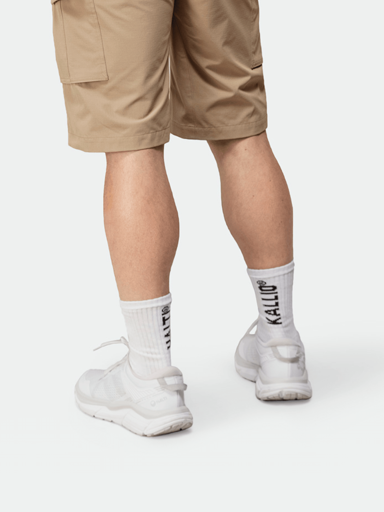 En person i bruna shorts, vita sneakers och Halti Kallio Strumpor – vita strumpor med KALLIO på ryggen.