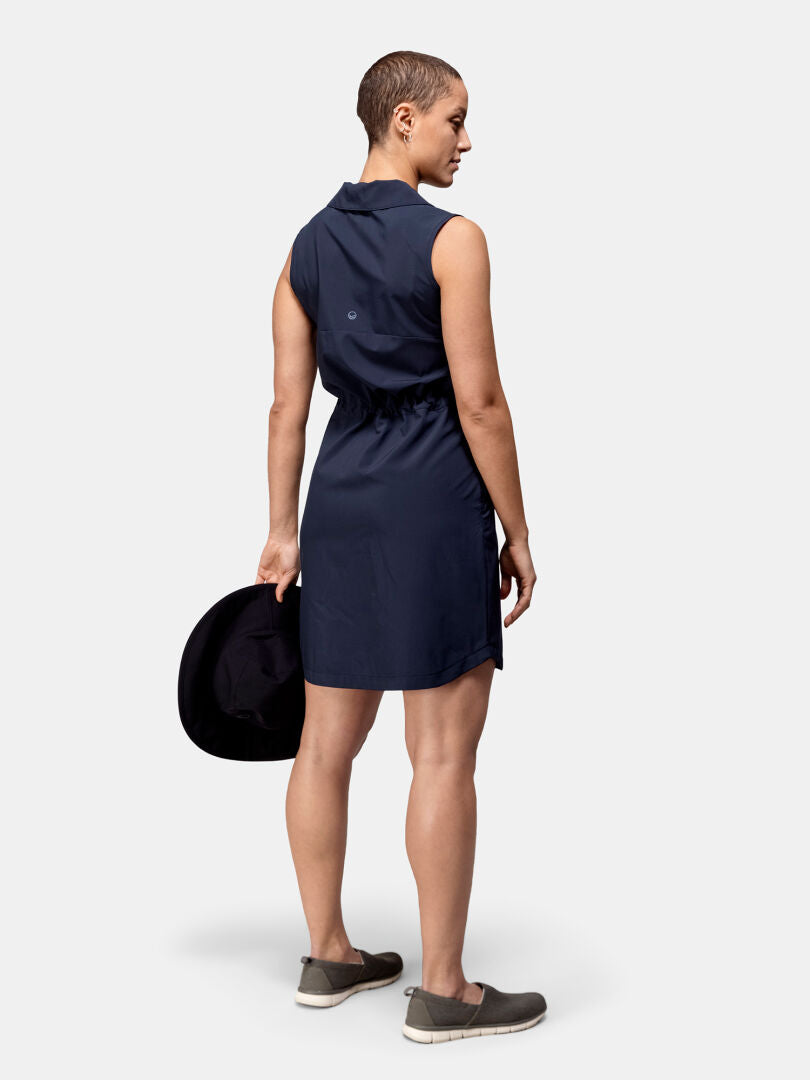 En person i en Halti Chipper X-stretch Klänning Dam står med ryggen mot kameran och håller i en svart hatt.