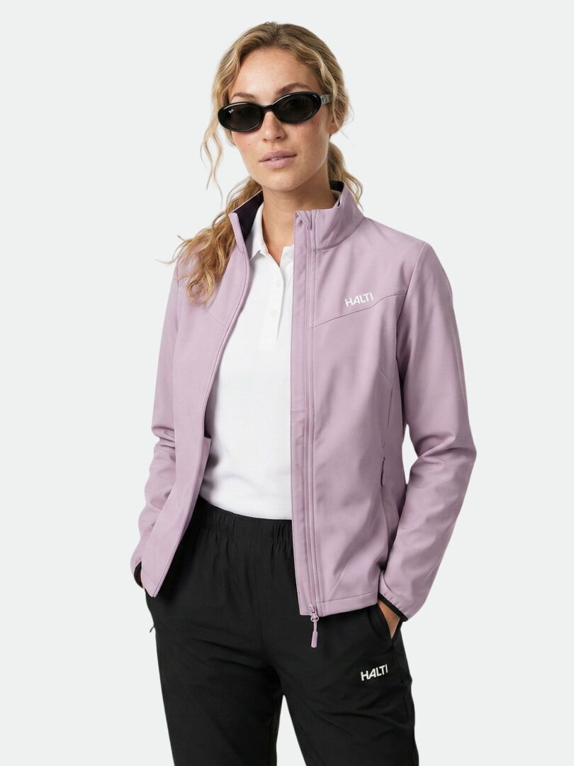 En kvinna med solglasögon bär Halti Wedge Softshell Jacka Dam, en vit skjorta och svarta byxor med händerna i fickorna.