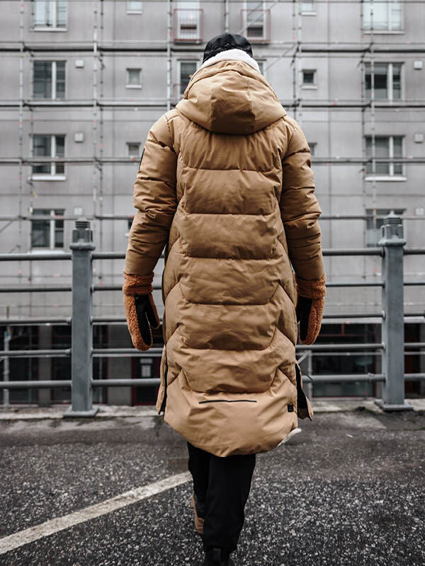 En person i Halti's Brahe Puffer Long Vinterjacka Dam och vantar går förbi ett hyreshus i staden.