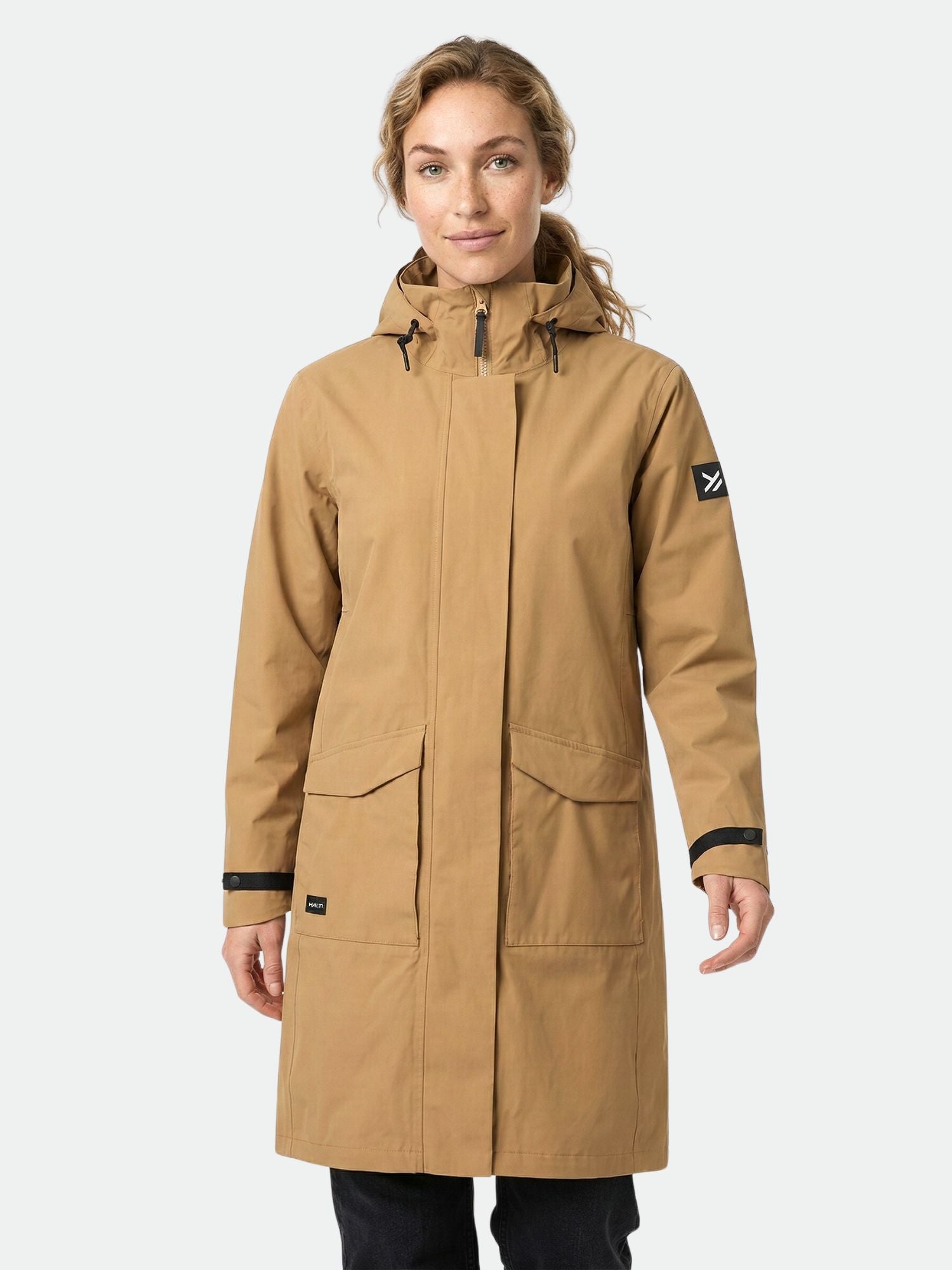 En person bär Halti Tokoi II DX Parkajacka Dam med framfickor och logopatch, mot en enfärgad bakgrund.