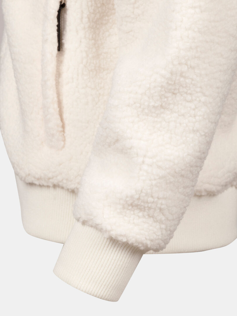 Närbild på Halti Lykky Fleece Jacka Dam i krämfärg, där man ser de ribbade ärmsluten och en delvis synlig ficka med dragkedja.