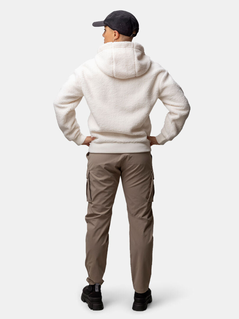 Person klädd i Halti Lykky Fleecejacka Dam, khakifärgade byxor, svarta skor och keps står med händerna på höfterna och ryggen mot kameran.