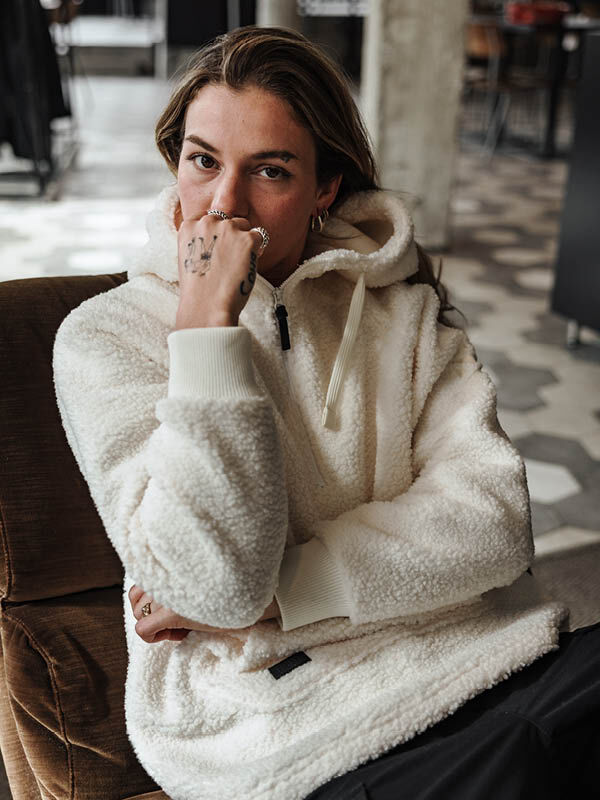 Person i Halti Lykky fleecejacka dam av återvunnen polyester sitter inomhus och tittar in i kameran med handen nära munnen.