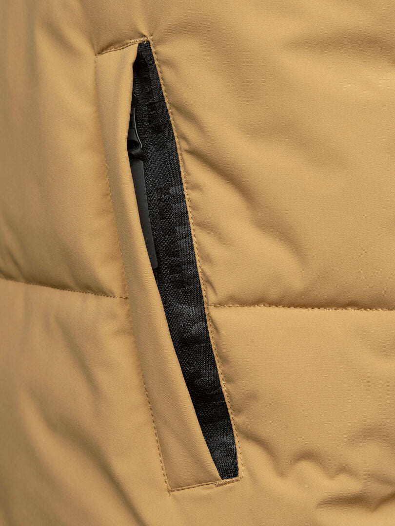 Närbild på Halti Penger Classic Puffer Väst Herr i beige med en svart ficka med dragkedja och svarta tygdetaljer.