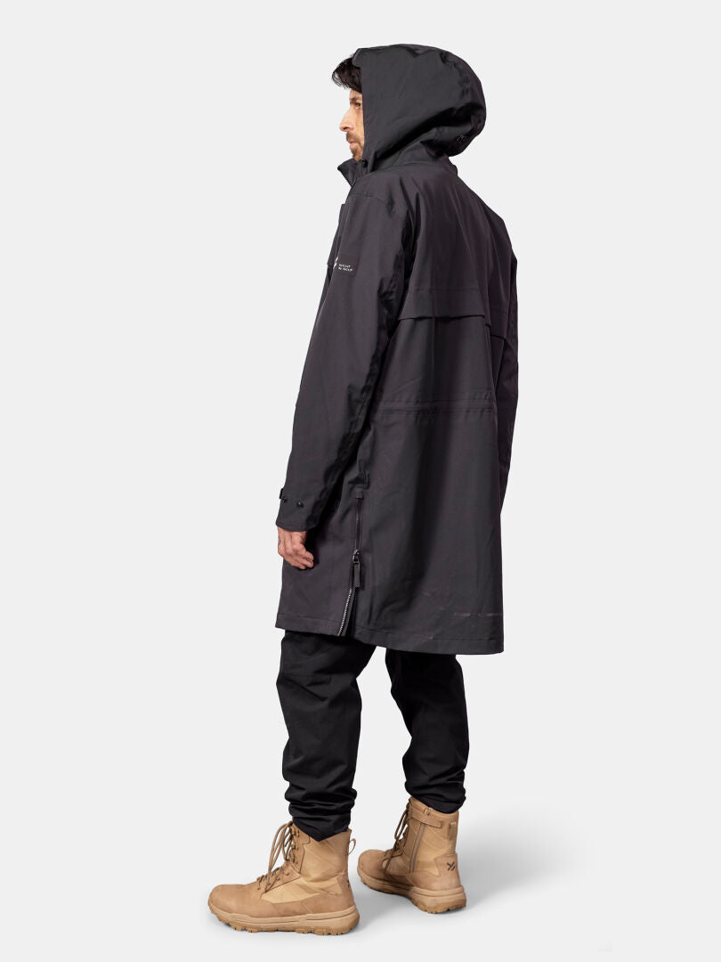 En man klädd i en Halti Tokoi II DX Parkajacka och beige stövlar står i sidoprofil mot en enfärgad bakgrund.