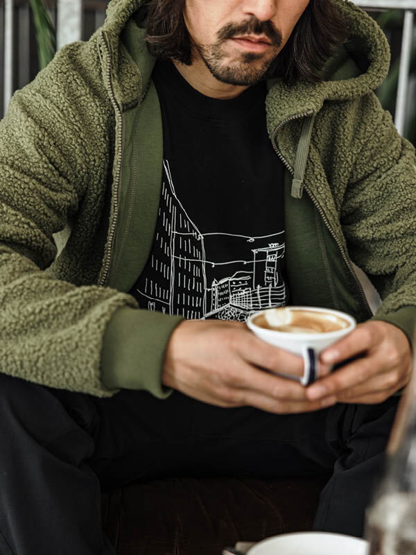 Iförd en Halti Lykky Fleecejacka Herr håller en person i en latte art coffee och kopplar av inomhus.