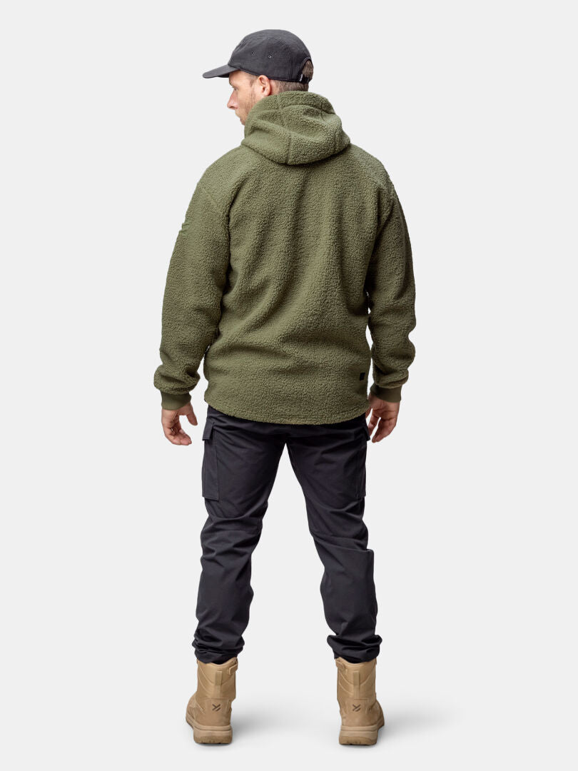 En man i Halti Lykky Fleecejacka Herr, tillverkad av återvunnen polyester, står med ryggen i svarta cargobyxor och solbruna stövlar.