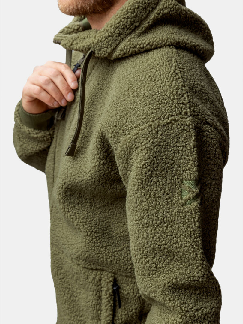 En person bär Halti Lykky Fleecejacka Herr, en olivgrön huvtröja i återvunnen polyester med dragkedja och uppdragen huva.