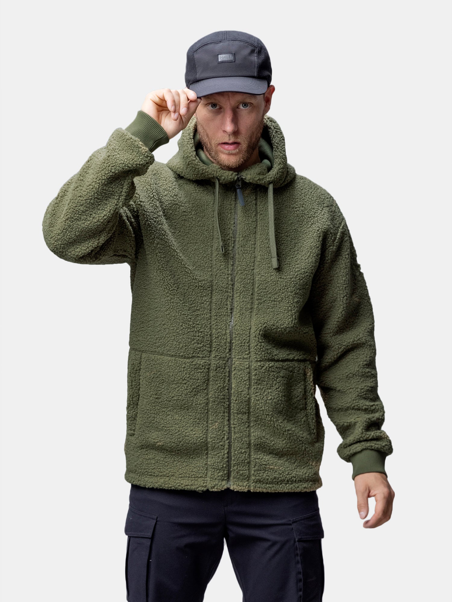 En person i Halti Lykky Fleecejacka Herr, tillverkad av återvunnen polyester, står och håller i brättet på en svart keps.