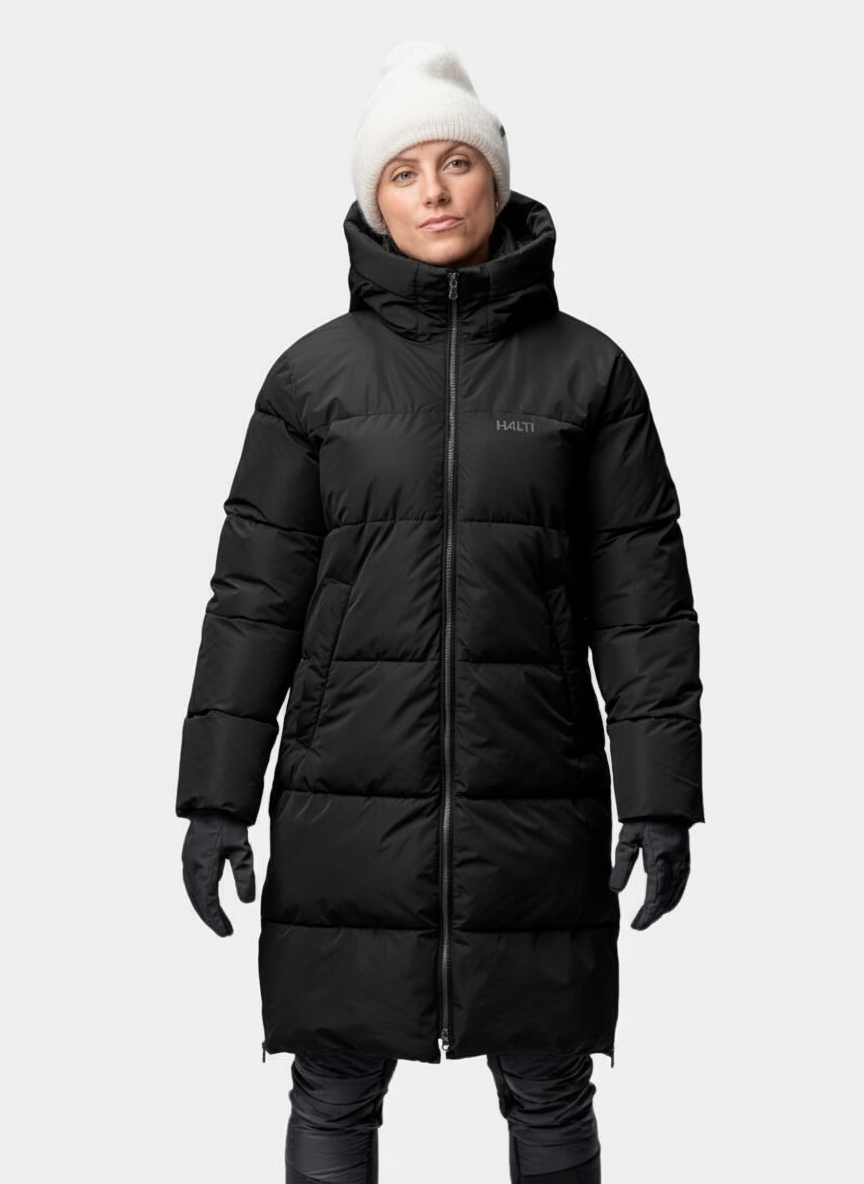 En person i Halti Sammal Vadderad Parkajacka Dam, vit stickad mössa, svarta handskar och mörka byxor står vänd framåt.