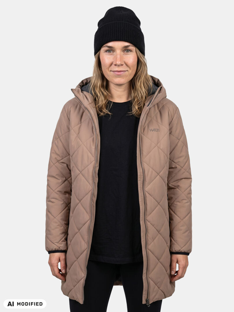 Modell klädd i Halti Haapa Vadderad Jacka Dam, svart tröja och mössa mot en enfärgad ljus bakgrund.