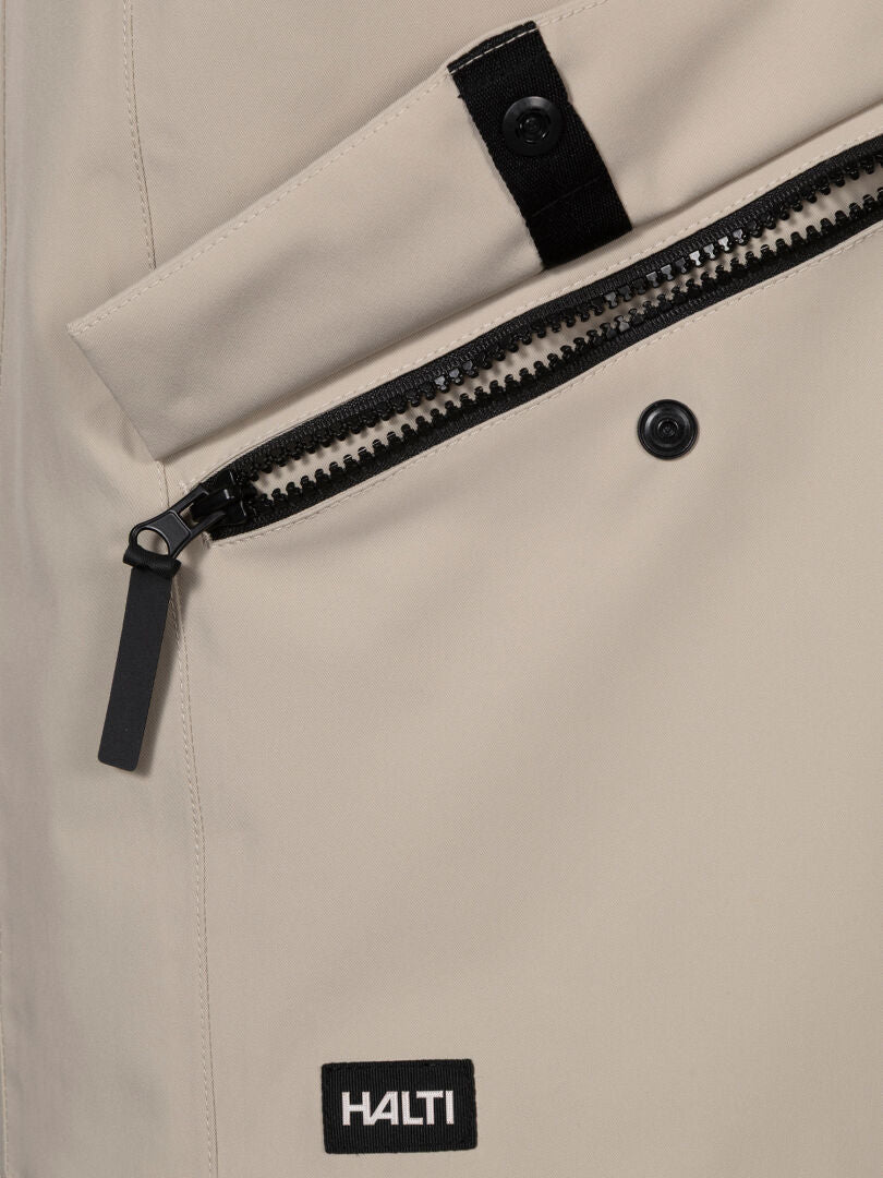 Närbild på Halti Tokoi DX Jacka Herr, beige, med DrymaxX-material, diagonal ficka med dragkedja och svart Halti-logopatch.