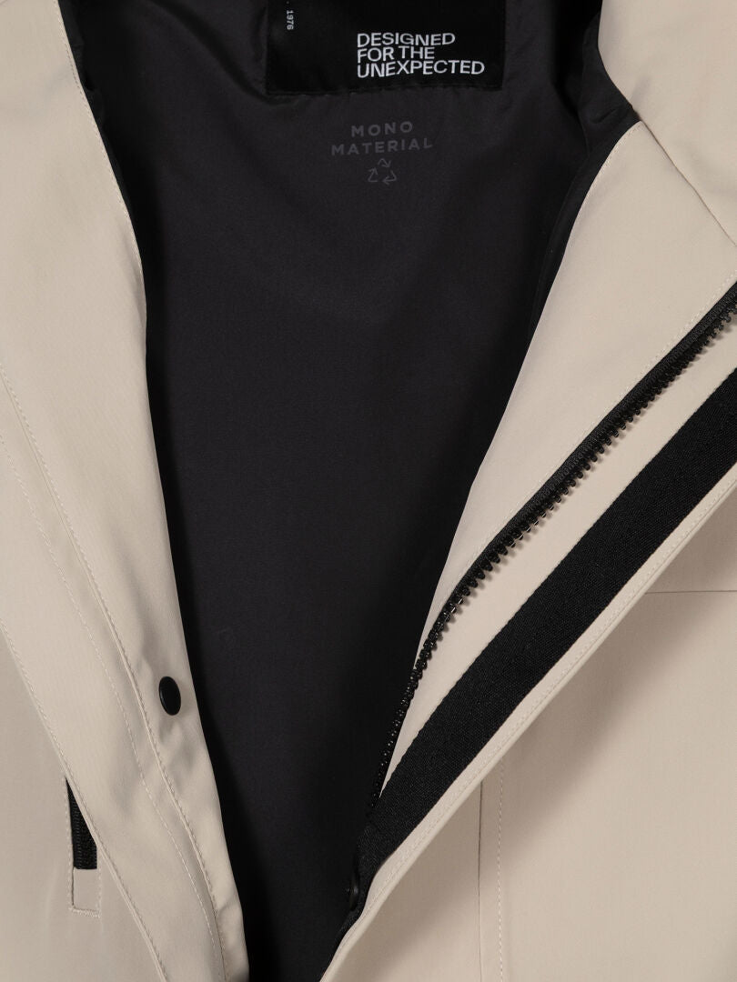 Närbild av Halti Tokoi DX Jacka Herr i beige med svart innerfoder, dragkedja och etiketten DESIGNED FOR THE UNEXPECTED.