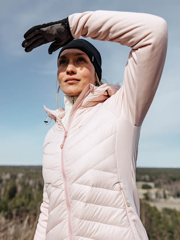 Kvinna i Halti Huippu Hybrid Dunjacka Dam, ljusrosa Pertex Quantum ripstop, skyddar sina ögon utomhus.