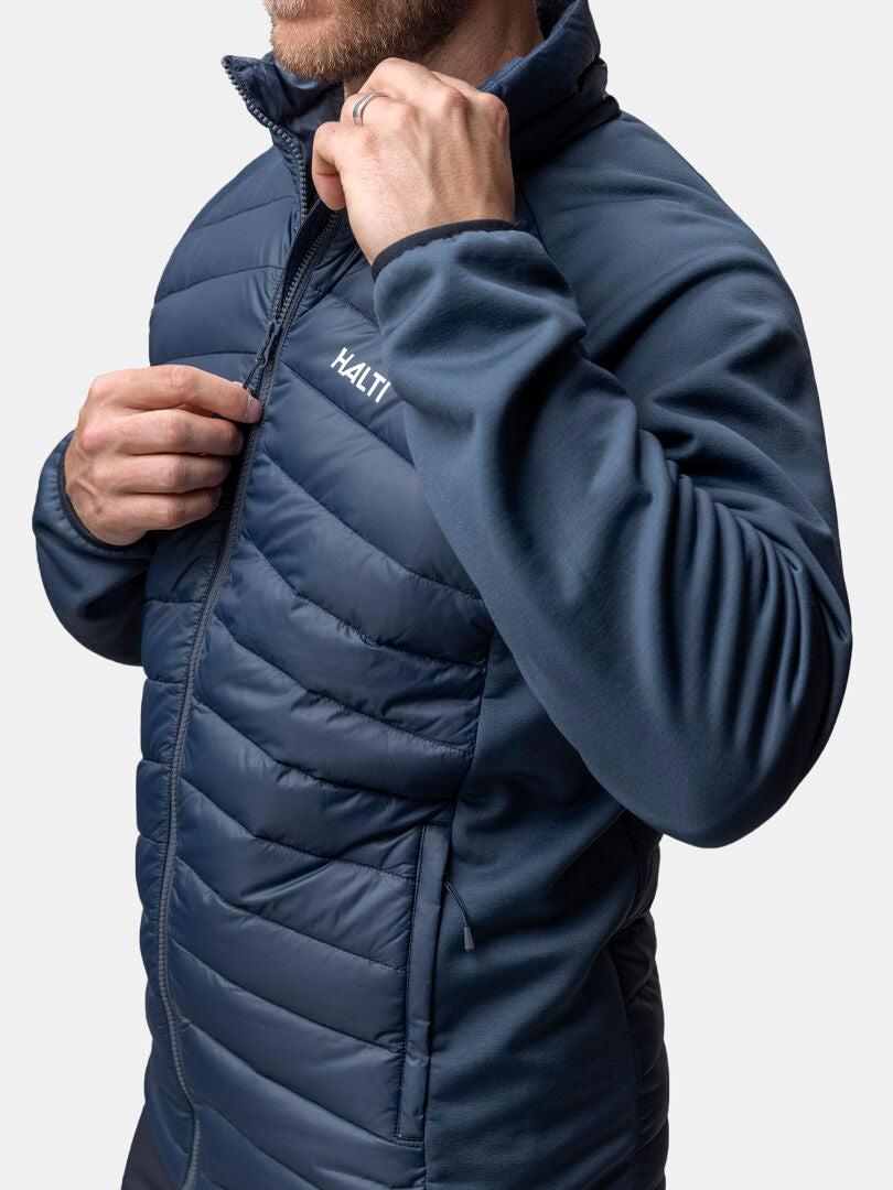 En person drar upp dragkedjan på Haltis Huippu Hybrid Dunjacka Herr i blått, tillverkad av Pertex Quantum-tyg.