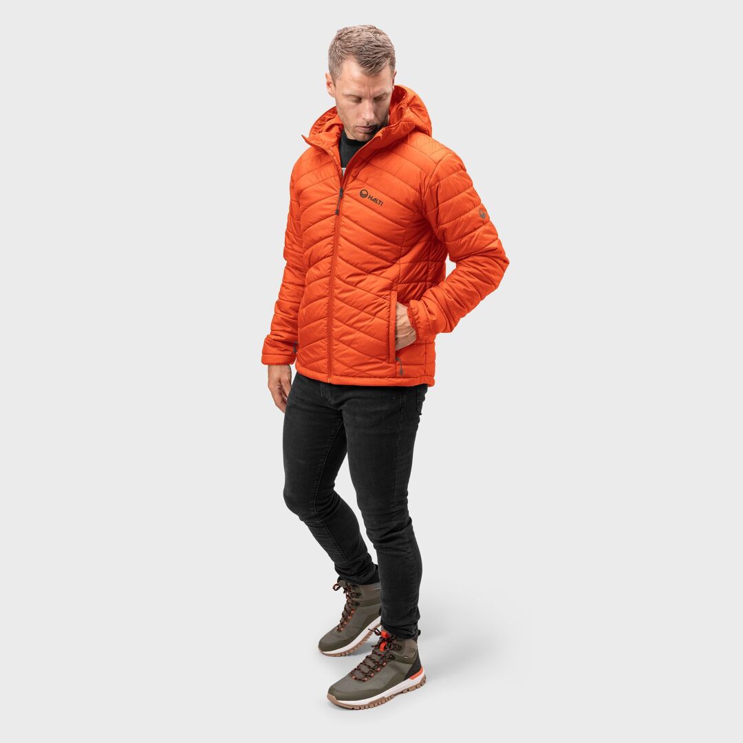 En man i en Halti Komu Lätt Vadderad Jacka Herr står i svarta jeans och gröna stövlar mot en vit bakgrund.
