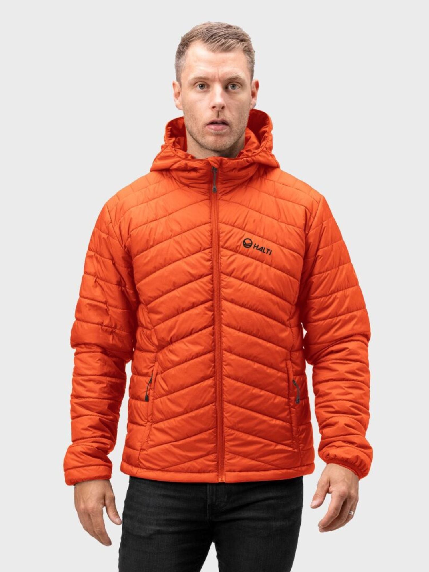 En person i en Halti Komu Lätt Vadderad Jacka Herr står mot en enkel, ljus bakgrund.