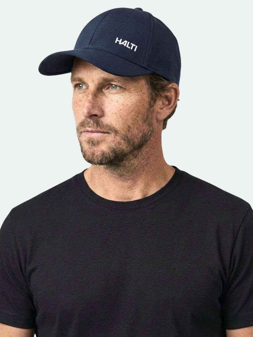 En man bär en marinblå Halti Mattas Baseball Keps UPF 50+ keps och en svart t-shirt och ser lite snett ut.