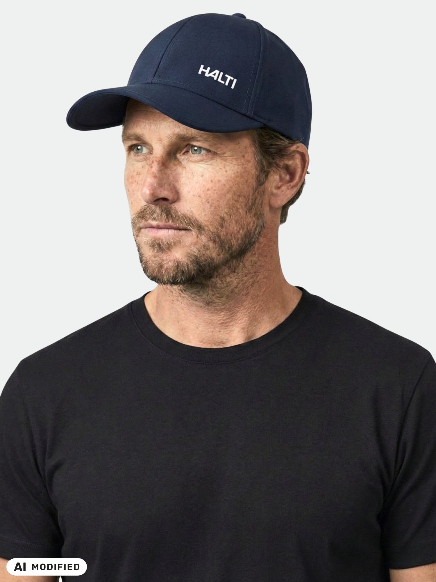 En man i en Halti Mattas-baseballkeps och svart t-shirt tittar åt sidan mot en enkel bakgrund. Kepsen torkar snabbt.