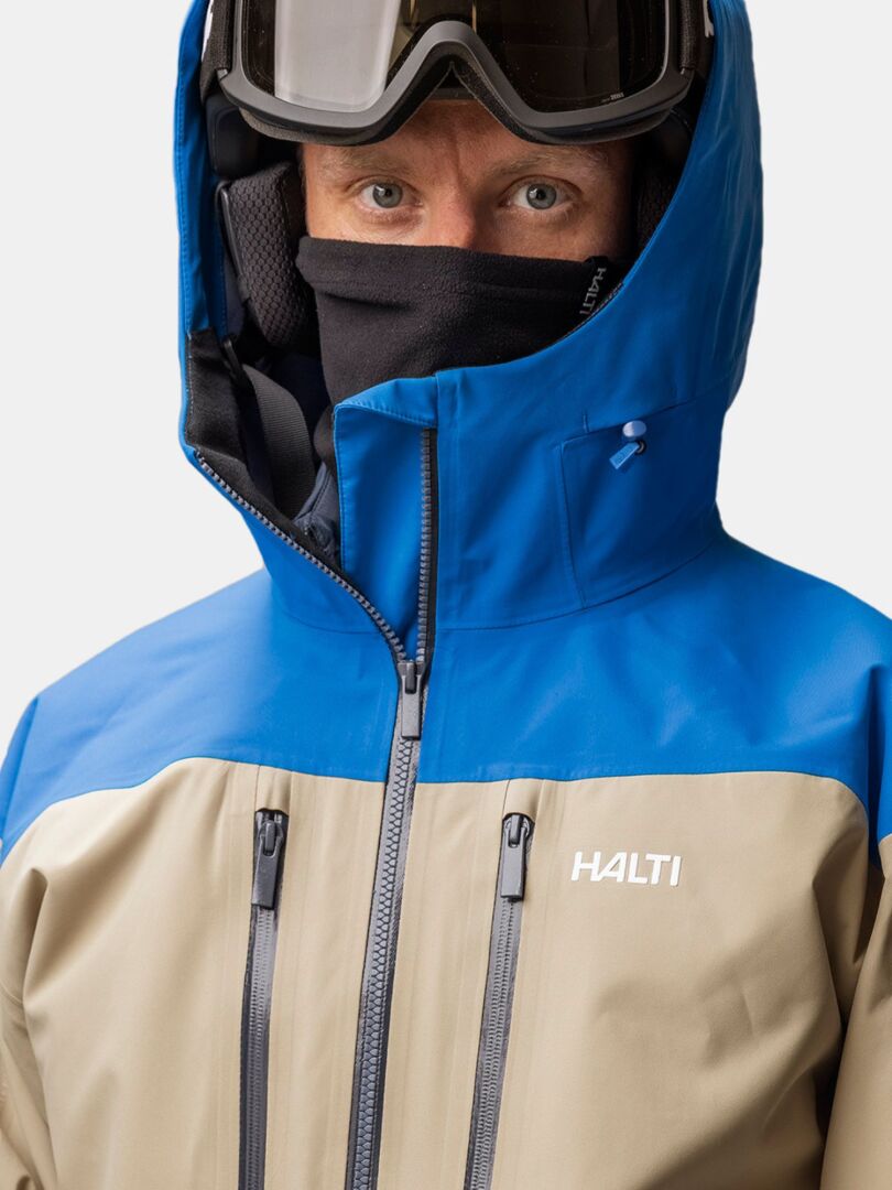 En person klädd i skidjacka, hjälm, skidglasögon och en svart Halti Trone Fleece Tubhalsduk-halsvärmare.