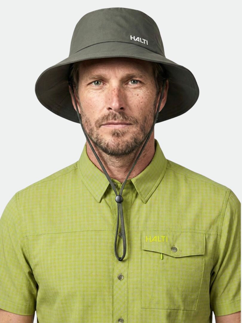 Man i grå Halti Luovi Hatt och grön kortärmad skjorta, vänd framåt mot en enfärgad bakgrund.