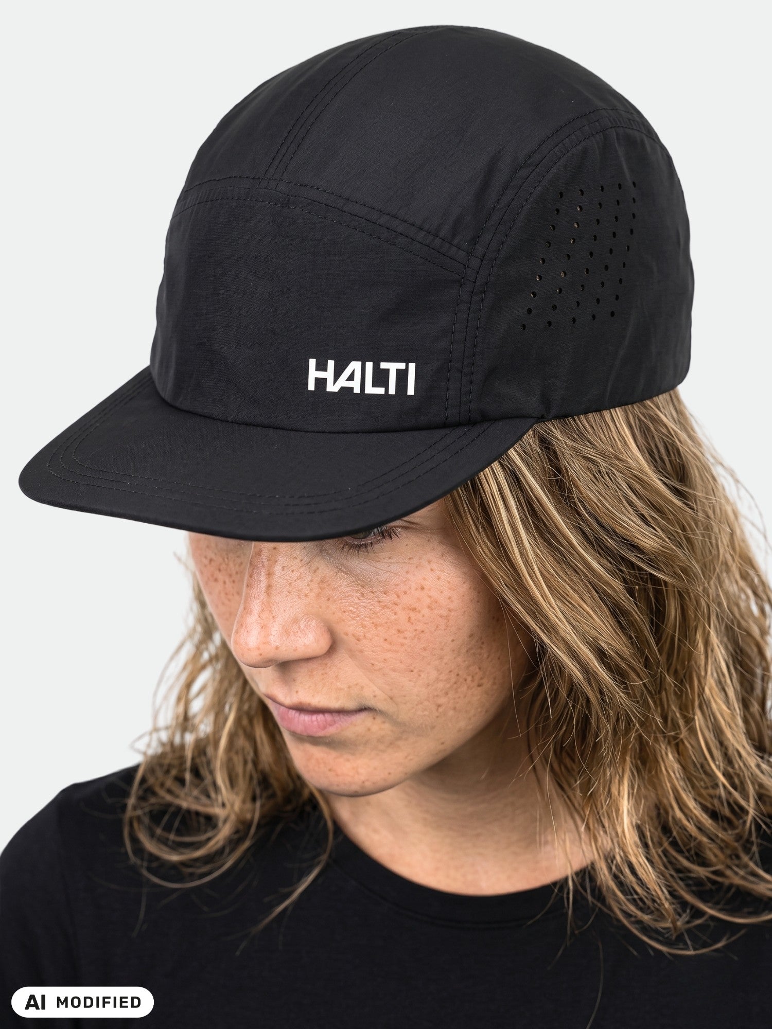 En person som bär Haltis Luovi Keps tittar nedåt; den svarta kepsen har ventilationshål och en vit logotyp.